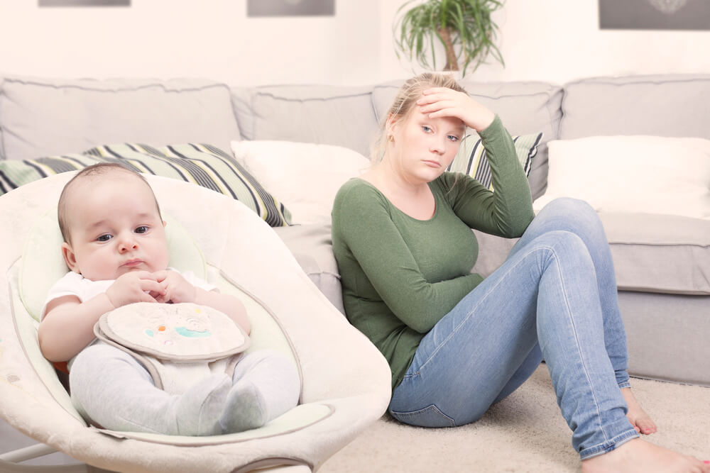 mulher em depressão pós-parto sentada no chão olhando para seu bebe