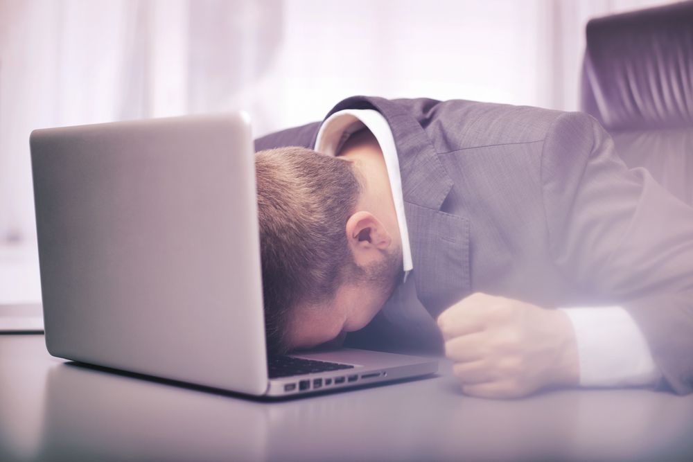 homem com a cabeça deitada em cima do computador com esgotamento profissional